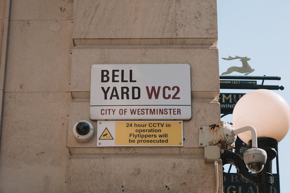A busy street scene near Westminster with a view of Big Ben in the background, featuring a variety of vehicles including buses, cars, and construction trucks. The roadway is lined with mature trees on